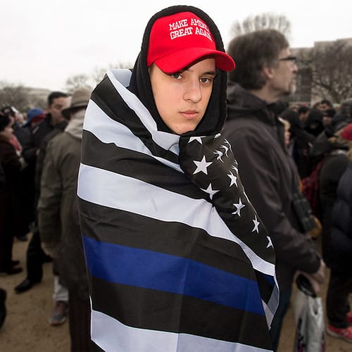 Man With MAGA hat and draped in "Thin Blue Line" American Flag