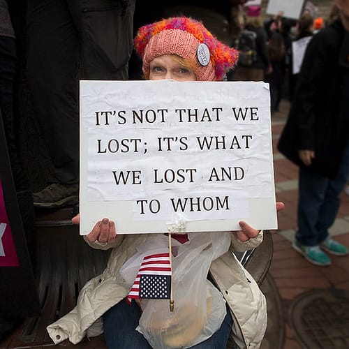 Woman holding sign: "It's Not That We Lost. It's What We Lost and To Whom"